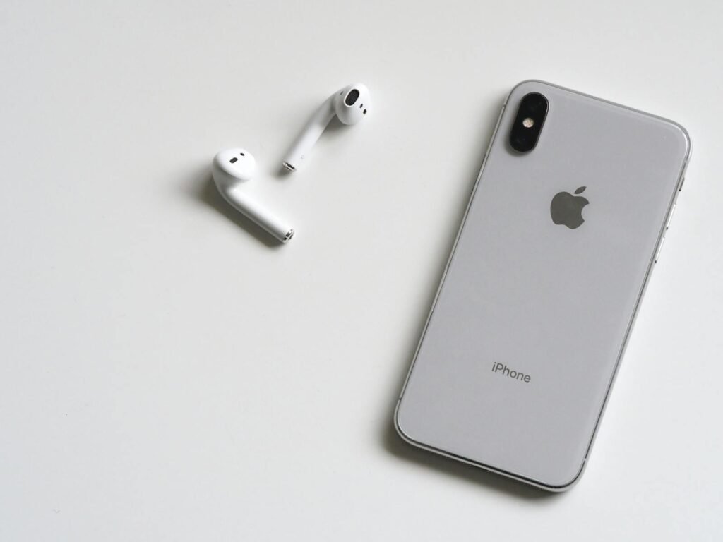 Close-up of a silver iPhone and wireless AirPods on a sleek white background.