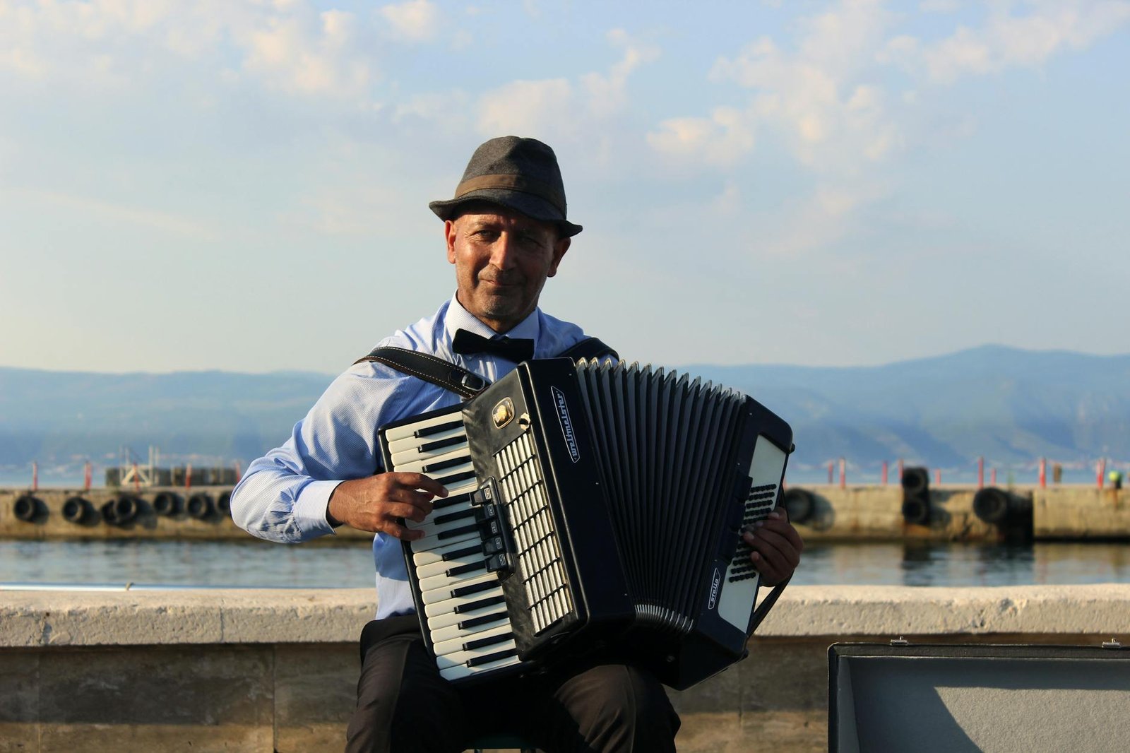 man playing accordion by waterfront